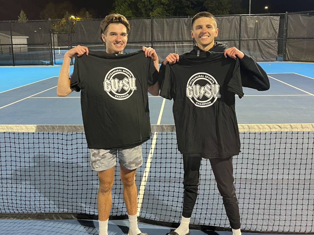 Students holding up championship shirts from a doubles tennis tournament